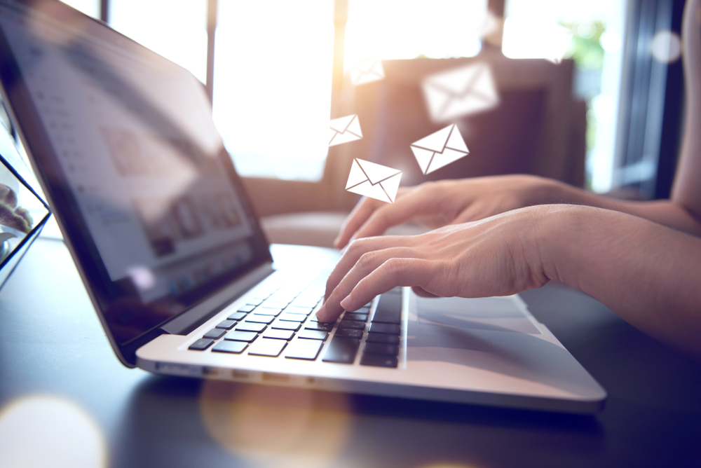 A person typing on a laptop with e-mail icons floating above the keyboard in warm natural light